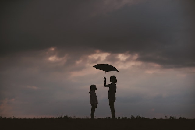 A storm in the background. A woman is holding an ubrella above a child.